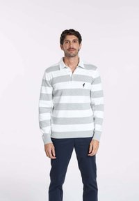 Pull de rugby ray é gris et blanc avec un col, des poignets côtelés et un petit logo sur la poitrine. Le modèle porte un pantalon bleu marine.