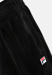 Sorte velour sweatpants med elastisk talje og sidelommer. Har broderet FILA-logo i rød, hvid og blå på venstre side.