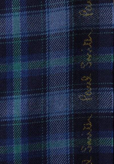 Μπλε και πράσινο καρό ύφασμα με λοξή υφαντική υφή και μικρό κίτρινο κεντημένο κείμενο κατά μήκος μιας άκρης.