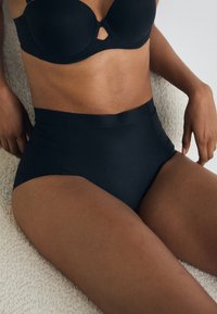 Chiloți negri cu talie înaltă, fabricați dintr-un material neted și elastic. Au un design fără cusături, cu cusături minime și o talie simplă.