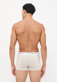Beige Tommy Hilfiger boxershorts med en mærket waistband, tætsiddende design og glat tekstur; båret af en person set fra ryggen.
