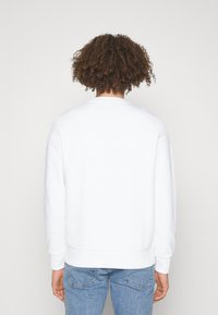 Felpa bianca con girocollo e polsini a costine, vista da dietro. Tessuto morbido, vestibilità casual, abbinata a jeans azzurri chiari.