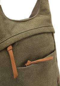Olive green canvas bag with a smooth texture, featuring a side pocket with a brown leather accent and a zipper pull tab.