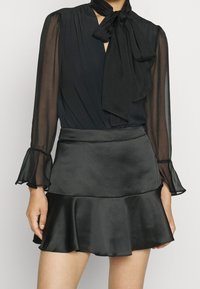 Black blouse with a tie detail at the neckline and sheer long sleeves, paired with a black satin flared mini skirt. Smooth texture.