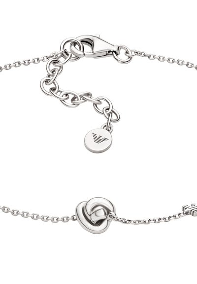Bracelet en argent avec un design de chaîne à maillons, un pendentif rond gravé du logo, et un détail distinctif en nœud. La texture du métal est lisse.