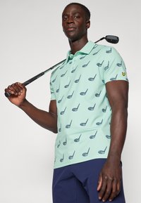 Light green polo shirt with a repeating golf club pattern, short sleeves, and a three-button placket. Worn with dark navy pants.