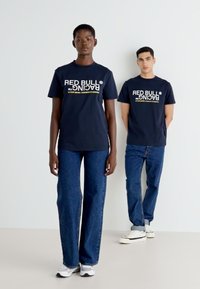 Mørkeblå bomulds t-shirts med "RED BULL RACING" trykt i hvid og gul logo. Styllet med blå jeans og casual sneakers.
