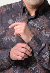 Bloemmotief shirt in donkere stof met tinten zwart, bruin en grijs. Kenmerkt zich door een button-down kraag en donkere knopen.