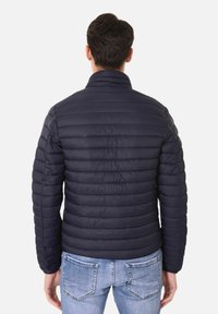 Giacca imbottita blu navy con motivo a righe orizzontali e colletto alto. Indossata con jeans azzurri, che evidenziano una vestibilità slanciata.