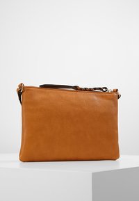 Ruskea nahkainen clutch-laukku, jossa on sileä pinta, suorakulmainen muoto, irrotettava punottu hihna ja hienovarainen kiilto. Vetoketjukiinnitys ylhäällä.
