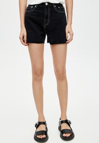 Zwarte denim shorts met een hoge taille en een rafelige zoom. Contraststiksel en vijf zakken. Gecombineerd met zwarte sandaaltjes met bandjes.