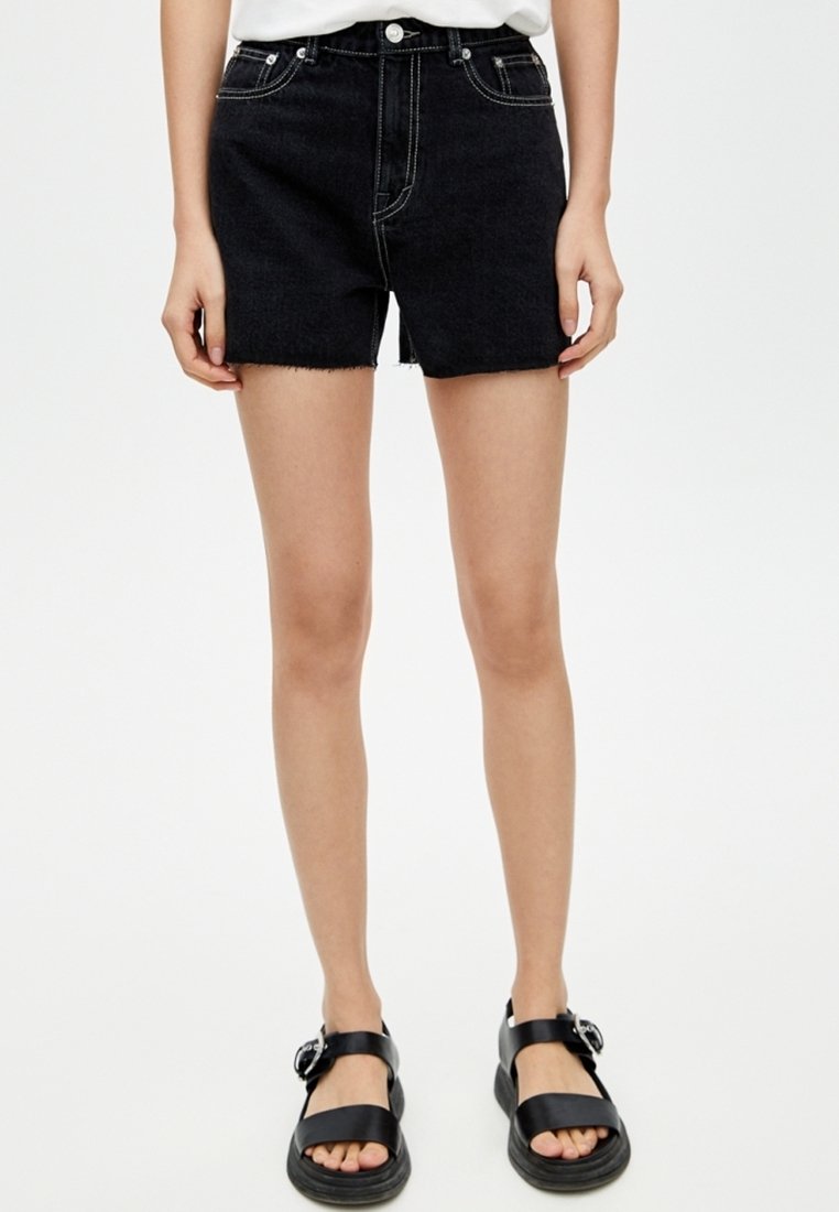 Zwarte denim shorts met een hoge taille en een rafelige zoom. Contraststiksel en vijf zakken. Gecombineerd met zwarte sandaaltjes met bandjes.