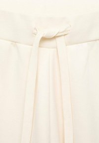 Pantalons beige clair en tissu doux et texturé, avec une taille élastique dotée d'un cordon de serrage et des plis subtils pour une touche de style supplémentaire.