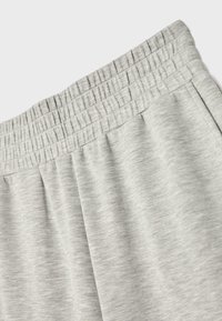 Pantalon de survêtement gris clair avec une taille élastique et des poches latérales, montré en gros plan avec la texture du tissu visible.