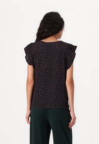 Top di tessuto nero con stampa floreale in rosa e bianco, maniche a farfalla, scollatura tonda e vestibilità ampia, abbinato a pantaloni verdi.