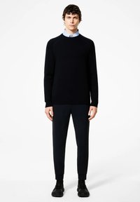 Zwart gebreid sweater met een ronde hals, geribbelde zoom en textuurdetails, gecombineerd met donkere broeken en zwarte sneakers. Blauw shirt eronder.