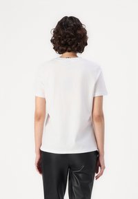 White cotton t-shirt with a crew neck, short sleeves, and a straight cut, paired with black faux leather pants. No visible logos or patterns.