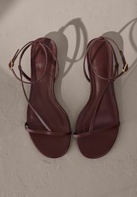 Sandalias planas burdeos con un diseño minimalista, que cuentan con tiras finas y una hebilla, textura suave y suela plana.