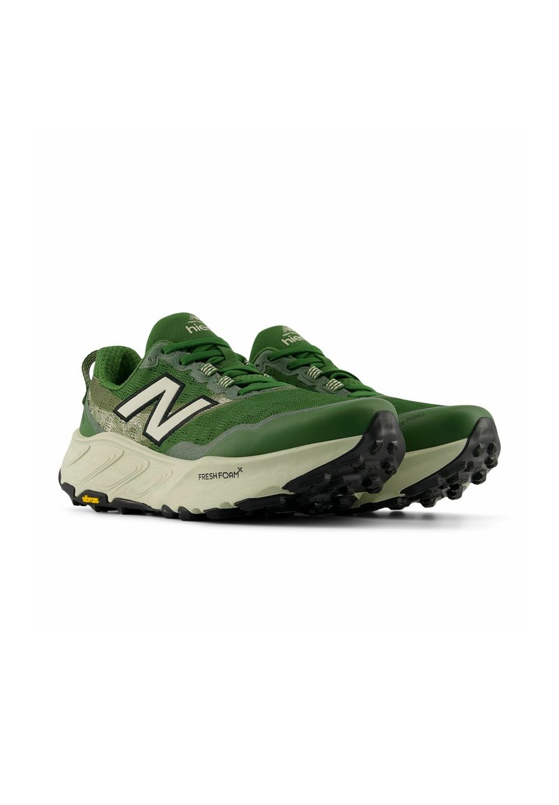 Ein Paar grüne und beige Trailrunning-Schuhe mit schwarzen Profilsohlen und einem weißen "N"-Logo an den Seiten, nach vorne geneigt auf einem weißen Hintergrund.