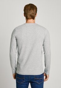 Grijze longsleeve t-shirt van zachte stof, met een ronde hals en een eenvoudige, gladde textuur, gecombineerd met donkerblauwe jeans.