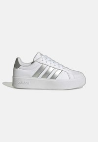 Witte sneakers met een glad, leren bovenwerk, drie metalen zilveren strepen aan de zijkant en een dikke witte zool. Voorzien van "adidas" branding.