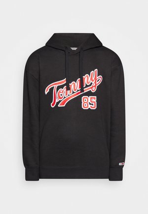Czarna bluza z kapturem z czerwonym i białym napisem „Tommy 85” na przodzie oraz małą naszywką z logo na mankiecie lewej rękawa.
