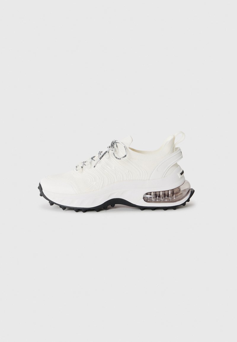 White athletic sneaker with black-tipped laces, textured knit upper, thick sole, visible air cushion in heel, and black tread sole.