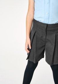 Pantaloni corti grigi a pieghe realizzati in un materiale testurizzato, abbinati a collant neri e una camicia a maniche corte azzurro chiaro con bottone davanti.
