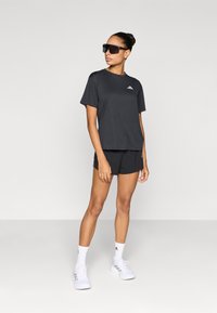 Zwart sportief T-shirt en korte broek set. Het T-shirt heeft een frontlogo, ontworpen voor actieve kleding, gecombineerd met witte sportschoenen en sokken.