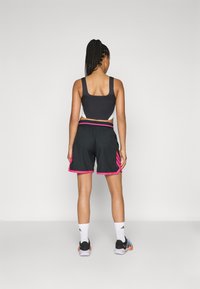 Sorte atletiske shorts med pink detaljer og elastisk talje, parret med en sort crop top, set fra ryggen. Fletninger synlige.