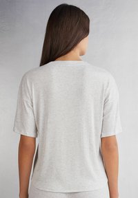 Světle šedé proužkované tričko s krátkým rukávem, kulatým výstřihem a mírně delším zadním lemem. Měkká bavlněná textura.