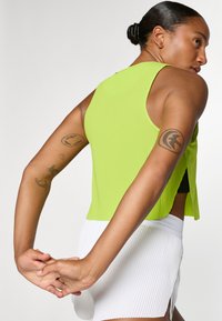 Lys grøn ribbet tanktop med en afslappet pasform og sideslids, parret med en plisseret hvid nederdel. Glat tekstur og moderne design.