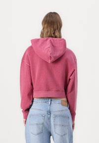 Felpa con cappuccio e orlo a coste in rosa polveroso, realizzata in un morbido cotone misto. Abbinata a jeans azzurri a vita alta.
