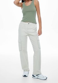 Lichtbeige cargobroek met grote zijzakken, knoopsluiting en een relaxte pasvorm. Gepaard met een aansluitend olijfgroen tanktop en witte sneakers.