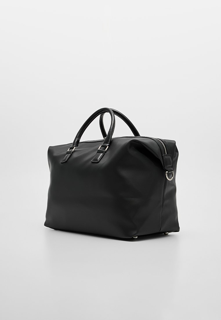 Bolsa de lona negra hecha de material liso y duradero. Cuenta con asas dobles, cierre de cremallera y detalles de herrajes metálicos.