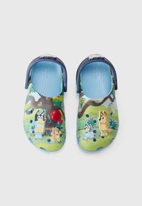 Zoccoli colorati per bambini con un design a cartoni animati blu e verde, che presenta personaggi di cani, alberi e fiori. Realizzati in materiale sintetico.