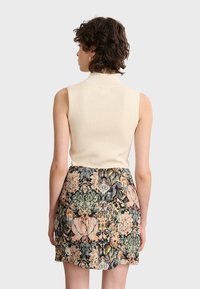 Cremfarbener, gerippter ärmelloser Oberteil, kombiniert mit einem strukturierten Blumenkleid in Rosa-, Grün- und Schwarztönen, das eine taillierte Silhouette aufweist.