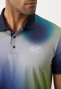Short-sleeve polo shirt in gradient blue and green fabric, featuring a navy collar, two buttons, and "EA7 Emporio Armani" logo.