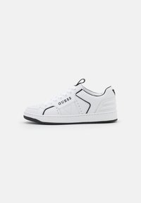Sneaker bianco con accenti neri e dettagli perforati. Presenta una suola in gomma testurizzata e chiusura con lacci, contrassegnata dal logo "GUESS".