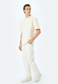 Crème korte mouwen T-shirt gecombineerd met lichtgekleurde denim broek en beige sneakers. De outfit heeft een ontspannen pasvorm en een minimalistisch ontwerp.