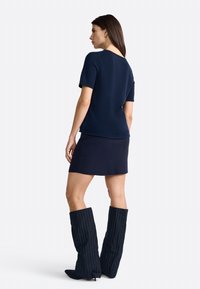 T-shirt tricot marine à manches courtes, associé à une jupe assortie et des bottes rayées jusqu'aux genoux, créant une présentation de tenue harmonisée.