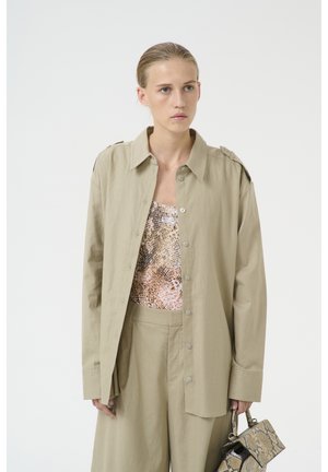 Light khaki oversized shirt with a button front, long sleeves, and shoulder epaulettes, paired with a textured snake-print top and pants.