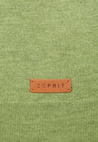 Grüner Strickstoff mit strukturiertem Finish und einem Lederlabel am unteren Rand, auf dem "ESPRIT" in blindgeprägten Buchstaben steht.