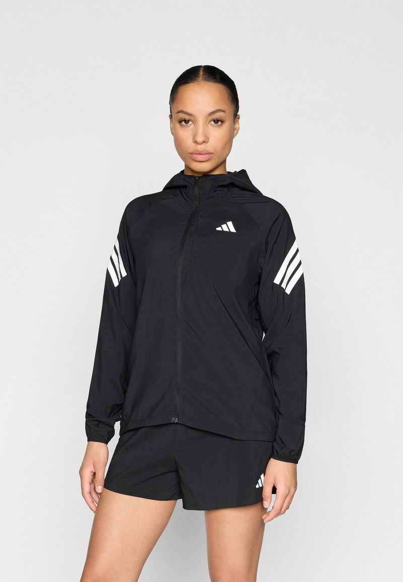 Chaqueta cortavientos negra con capucha, con detalles de tres franjas blancas en las mangas y logo en el pecho, fabricada con un material ligero.