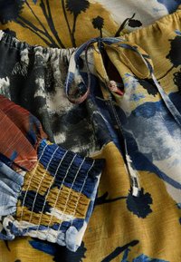 Tissu avec des motifs floraux et abstraits multicolores, doté d'un poignet froncé élastiqué et d'un cordon noué à la taille.