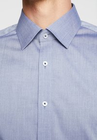 Lichtblauw overhemden met een subtiel gestreept patroon, gestructureerde kraag en witte knopen met een donkerblauw accent.