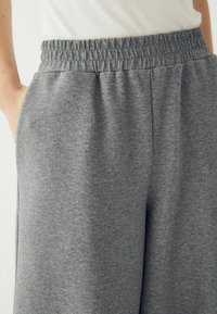 Szürke melegítőnadrág elasztikus derékkal, oldalsó zsebbel és puha textúrával. Jellemzője a laza szabás és a könnyű anyag.