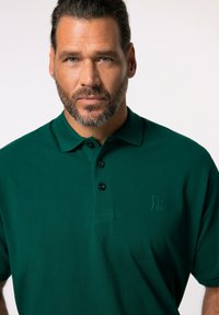 Grön polo t-shirt med en mjuk textur, tre-knapp placket och en diskret broderad logotyp på bröstet. Klassisk kragdesign.