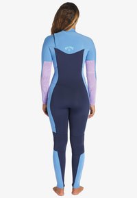 Traje de neopreno con paneles azules y marinos, con mangas de un tono morado claro texturizado, diseño ajustado, costuras planas y abertura redonda en la parte trasera del cuello.