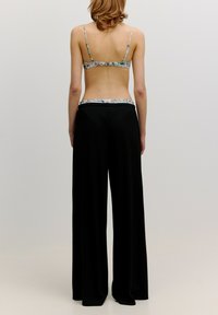 Zwarte wijde broek met een gestructureerde afwerking, voorzien van een bloemenbedrukt tailleband. De top is een bloemenpatroon bh met dunne bandjes.